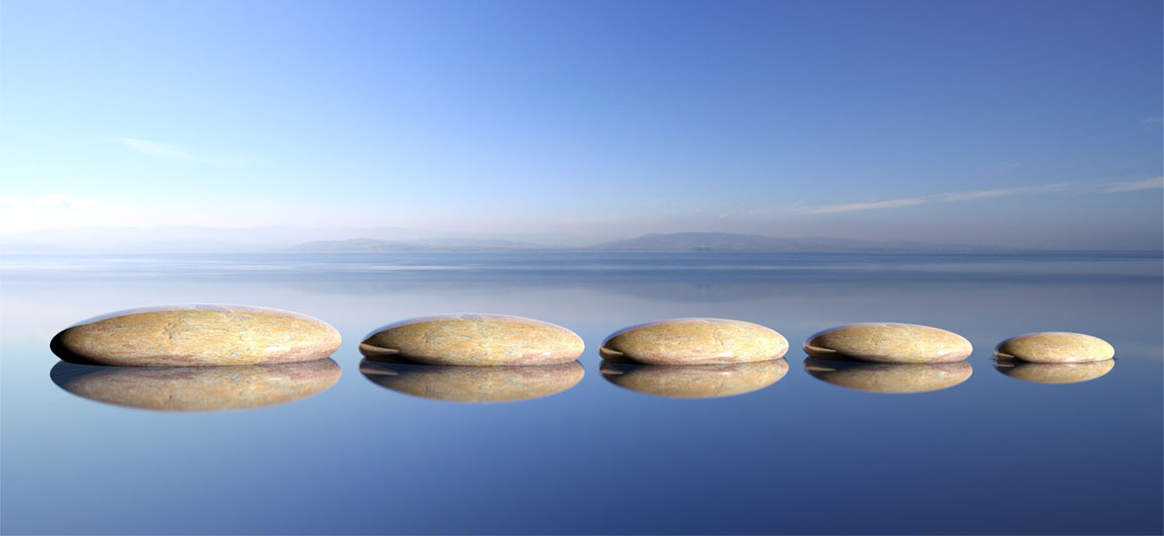 Zen stones row from large to small in water with blue sky and p